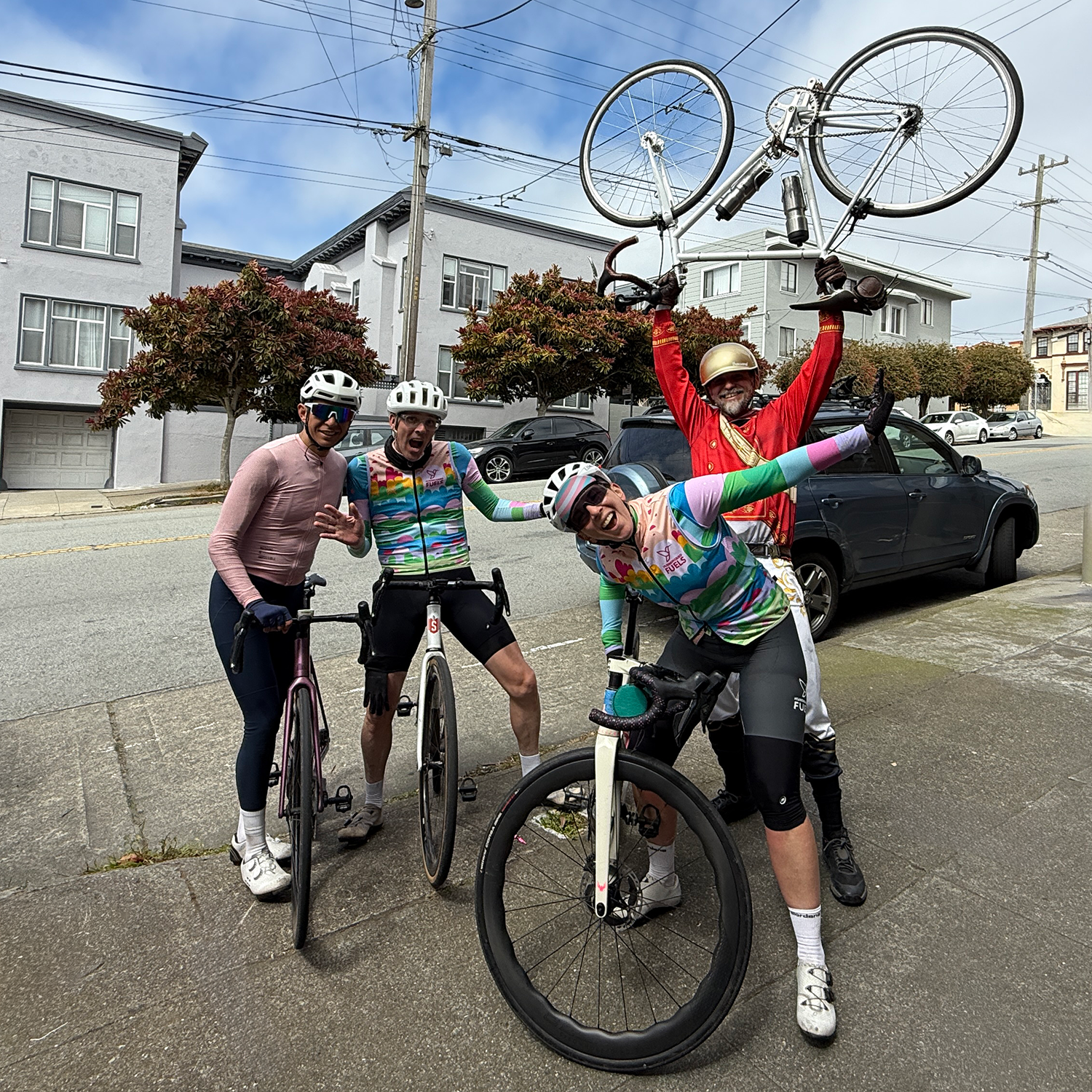 Four cyclists posing on a street with bicycles, wearing colorful outfits and helmets.
