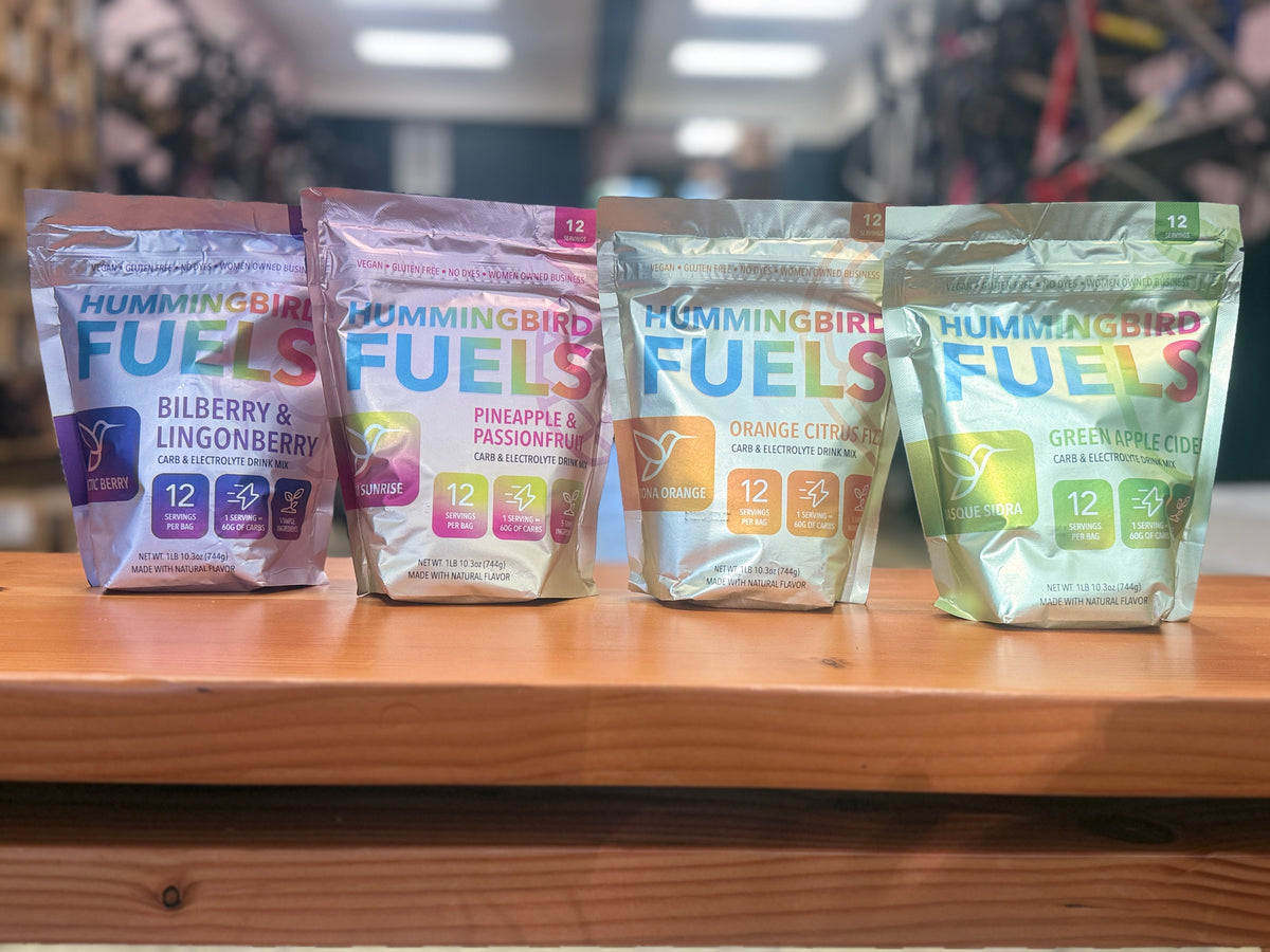 Four Hummingbird Fuels Big Bags are lined up on a wooden counter in a store setting. 