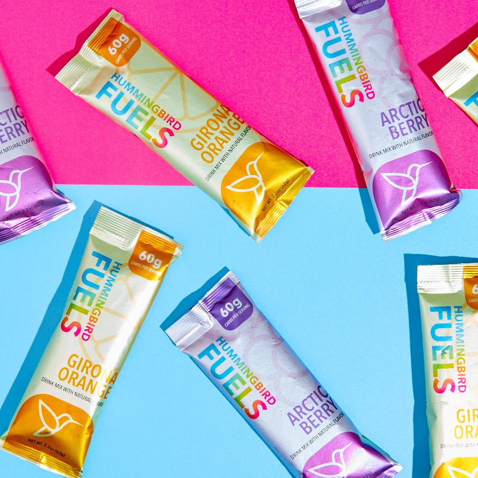 Hummingbird Fuels Single Serve Sachets arranged on a pink and blue background