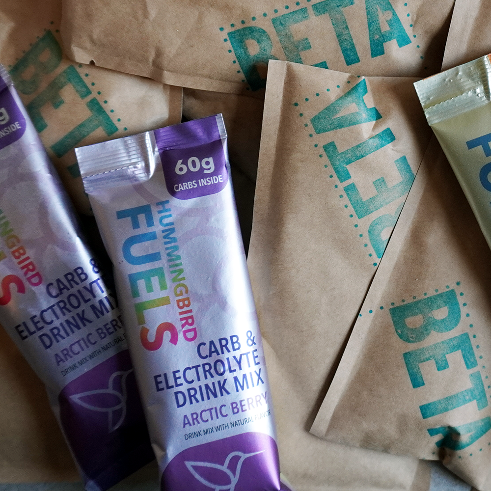Hummingbird Fuels Magic Gel BETA packets with a representative Arctic Berry single serve Sachet and container on a textured surface
